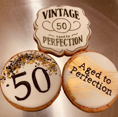 three decorated cookies sitting on top of a silver table next to each other with the number 50 written on them