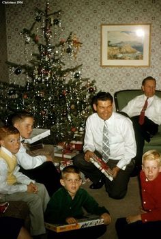 a group of people sitting in front of a christmas tree with presents on the floor