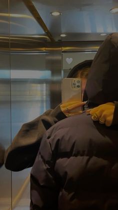 a person in a jacket and yellow gloves using a cell phone on a subway train