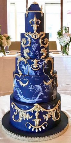 a three tiered blue and gold wedding cake sitting on top of a white table