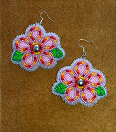 pair of pink flower beaded earrings with green leaves on brown carpeted surface, top view