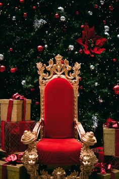 a red chair sitting in front of a christmas tree with presents around it and a gold crown on top