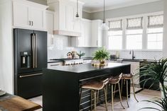 a kitchen with white cabinets and black counter tops, two stools are in front of the island