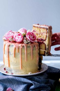 someone is cutting into a cake with pink flowers on the top and icing drizzled over it