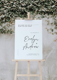 an easel stands in front of a white wall with greenery on the side