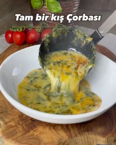 a white bowl filled with cheese and sauce on top of a wooden table next to tomatoes