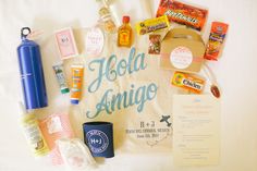 an assortment of food and drinks laid out on top of a white bed sheet with the words hello amigo written in blue