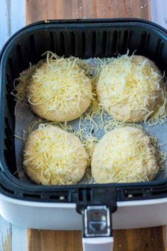 four uncooked pizzas in a plastic container on a cutting board with grated cheese