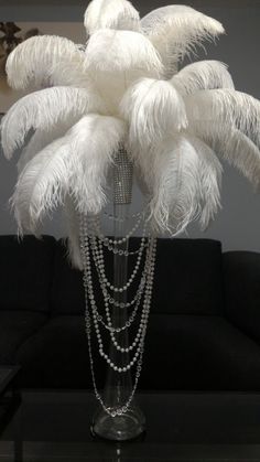 a vase filled with white feathers on top of a black table next to a couch