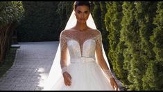 a woman in a wedding dress standing next to a tree and bushes with her hands on her hips