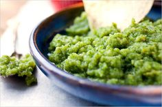 a bowl filled with green food next to a spoon