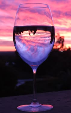 a wine glass sitting on top of a table next to a window with sunset in the background