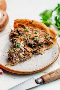 a slice of mushroom and parsley pie on a plate next to a knife, fork and sprig of parsley