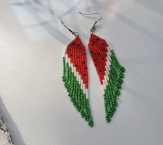 a pair of red, white and green seed beaded earrings on top of a table