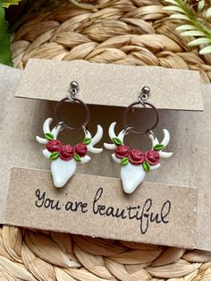 the earrings are decorated with red roses and white antlers, while the words you're beautiful appear to be written on them