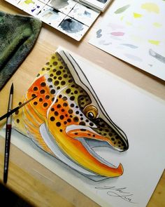 a painting of a fish on a table with watercolors and paintbrushes