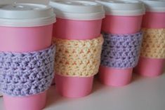 six coffee cups with crocheted lids lined up