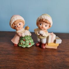 two little figurines sitting on top of a wooden table next to each other