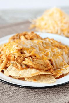 a white plate topped with nachos covered in cheese and shredded meat on top of tortilla chips