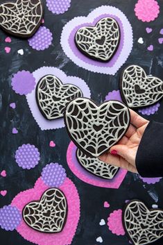 someone is holding some heart shaped cookies on a black surface with pink and purple hearts