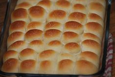 a pan filled with bread rolls on top of a wooden table next to a red and white checkered cloth