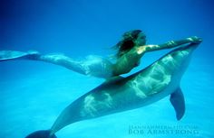 a woman is swimming in the water with a dolphin behind her and holding on to it's tail