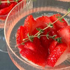 some strawberries are in a wine glass with ice and sprigs on top