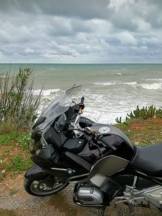 a motorcycle parked on the side of a road next to the ocean with waves in the background