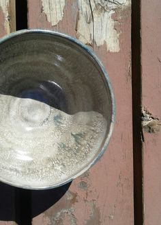 a metal bowl sitting on top of a wooden table next to a wall with peeling paint