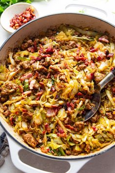 a pan filled with cabbage and meat on top of a white table next to other dishes