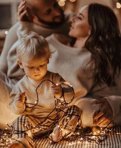 a woman and her baby are sitting on the floor with christmas lights all around them