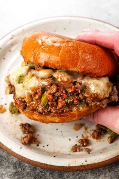 a hand holding a sandwich on top of a white plate with meat and cheese in it