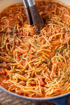 a pot filled with spaghetti and sauce on top of a wooden table