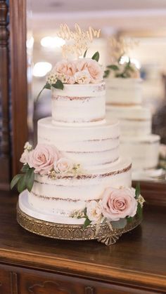 a white wedding cake with pink flowers and greenery sits on a table in front of a mirror