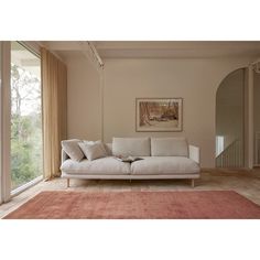 a living room with a white couch and red rug on the hardwood floor next to a large window