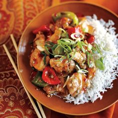 a brown plate topped with chicken and vegetables on top of rice next to chopsticks