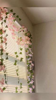 pink flowers hanging from the side of a window sill in front of a blinds