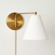 a gold wall light with a white shade on the side and a wooden stick attached to it