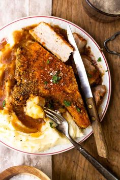 a white plate topped with mashed potatoes covered in gravy next to a knife and fork