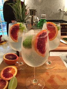 three glasses filled with different types of drinks on top of a cutting board next to sliced fruit