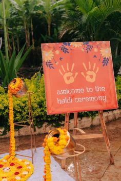 a welcome sign with flowers on it and a pole in the foreground that says welcome to the haldi ceremony