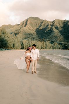 a man and woman are walking on the beach with mountains in the backgroud