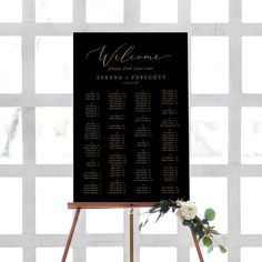 a black and gold wedding seating sign with white flowers on the table next to it