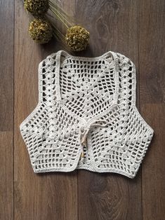 a white crocheted top sitting on top of a wooden floor next to dried flowers