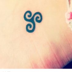 a small tattoo on the ankle of a woman's foot with an omen symbol