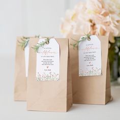 two brown paper bags with tags on them sitting next to a vase filled with flowers