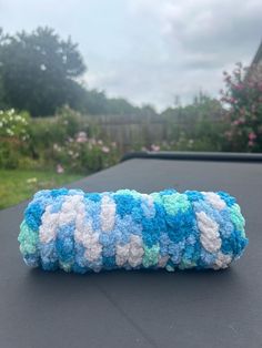 a blue and white crocheted object sitting on top of a black table outside