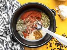 a pot filled with spices and seasoning next to garlic flakes on a yellow surface