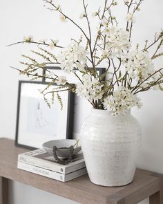 a white vase filled with flowers sitting on top of a wooden table next to a framed photograph