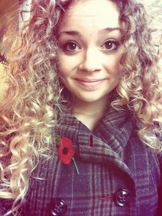 a woman with long curly hair and a flower in her lapel is smiling at the camera